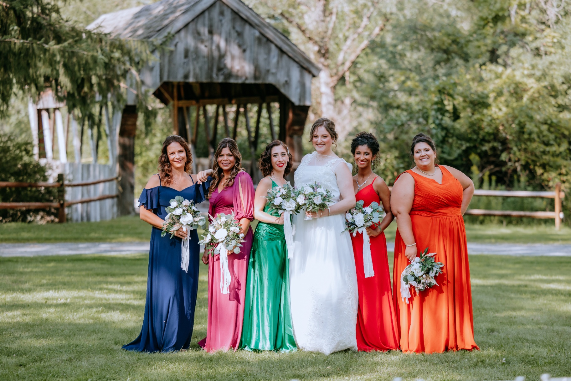 Bridesmaids in jewel-tone gowns at the covered bridge